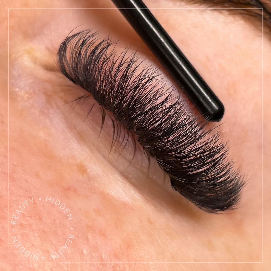 Eyelash extension application with a brush on a close-up of an eye.