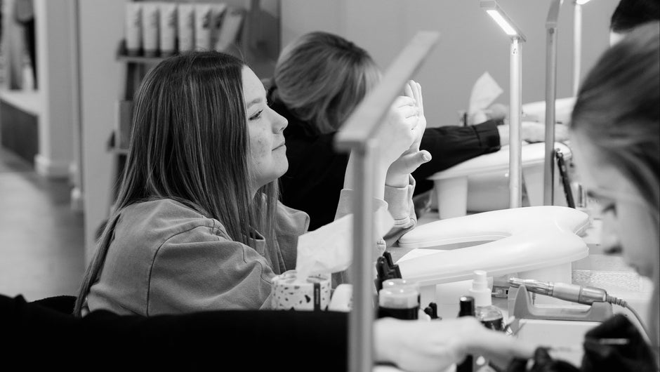 Nail salon with multiple clients receiving manicures, black and white photo.