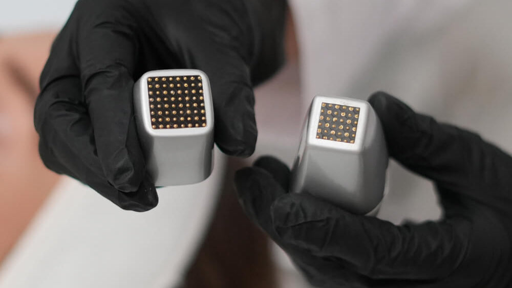 Person wearing black gloves holding two metallic devices with a grid pattern.